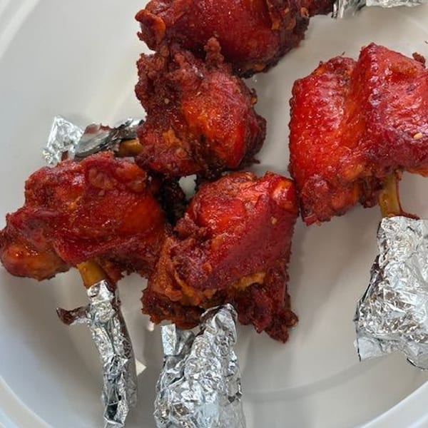 Close-up of Chicken Lollypop, a popular Indian appetizer, with foil-wrapped bones on a white plate.